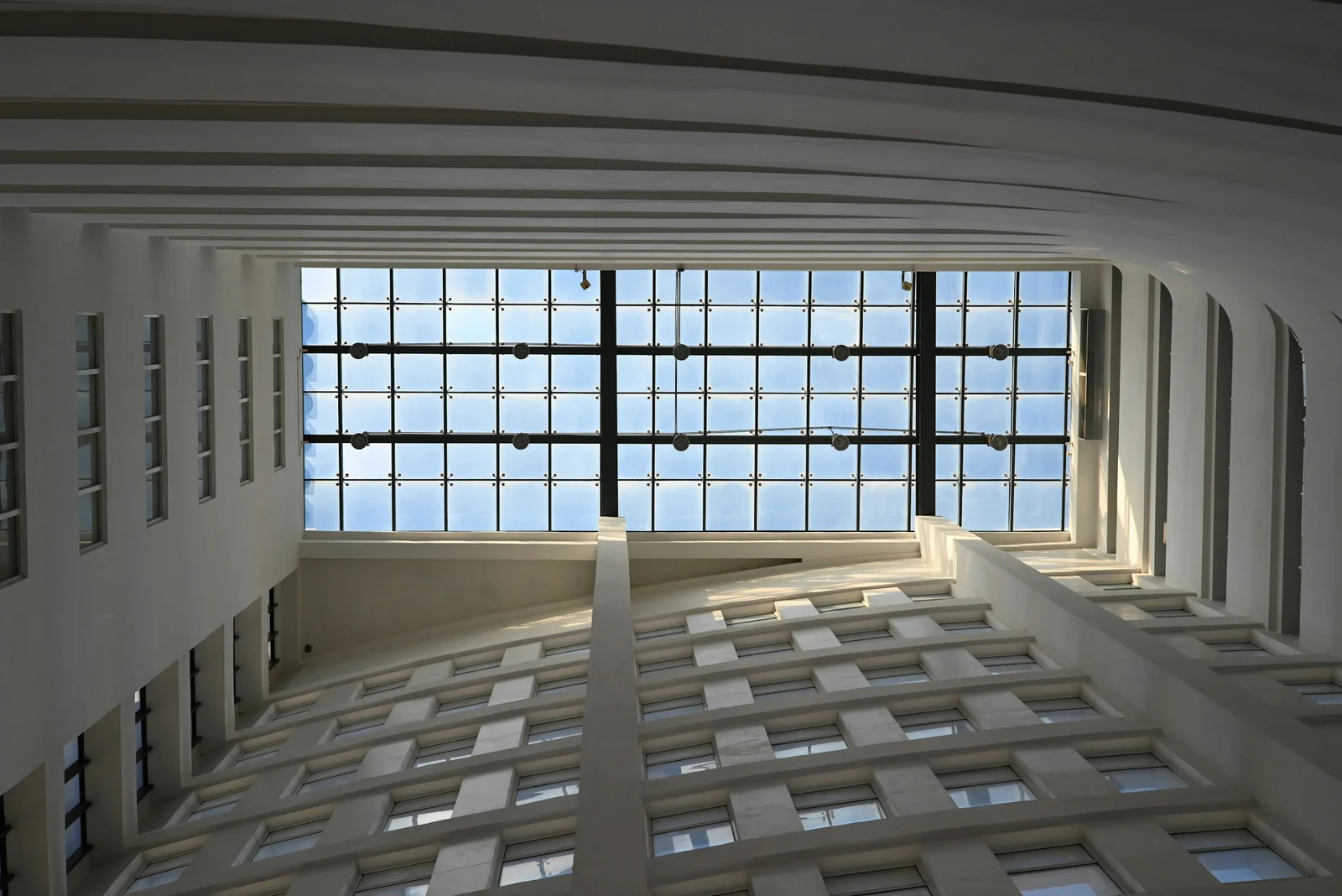 Atrium blanc d’un immeuble de bureaux, sous une verrière quadrillée baignée de lumière