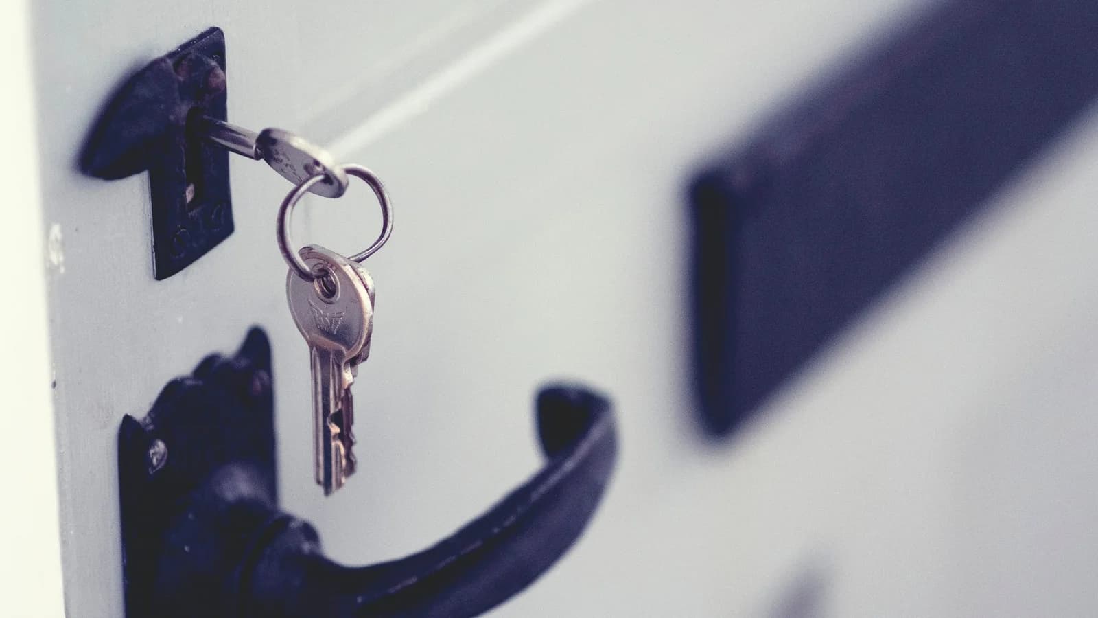 Trousseau de clés engagé dans la serrure d’une porte blanche à poignée noire.