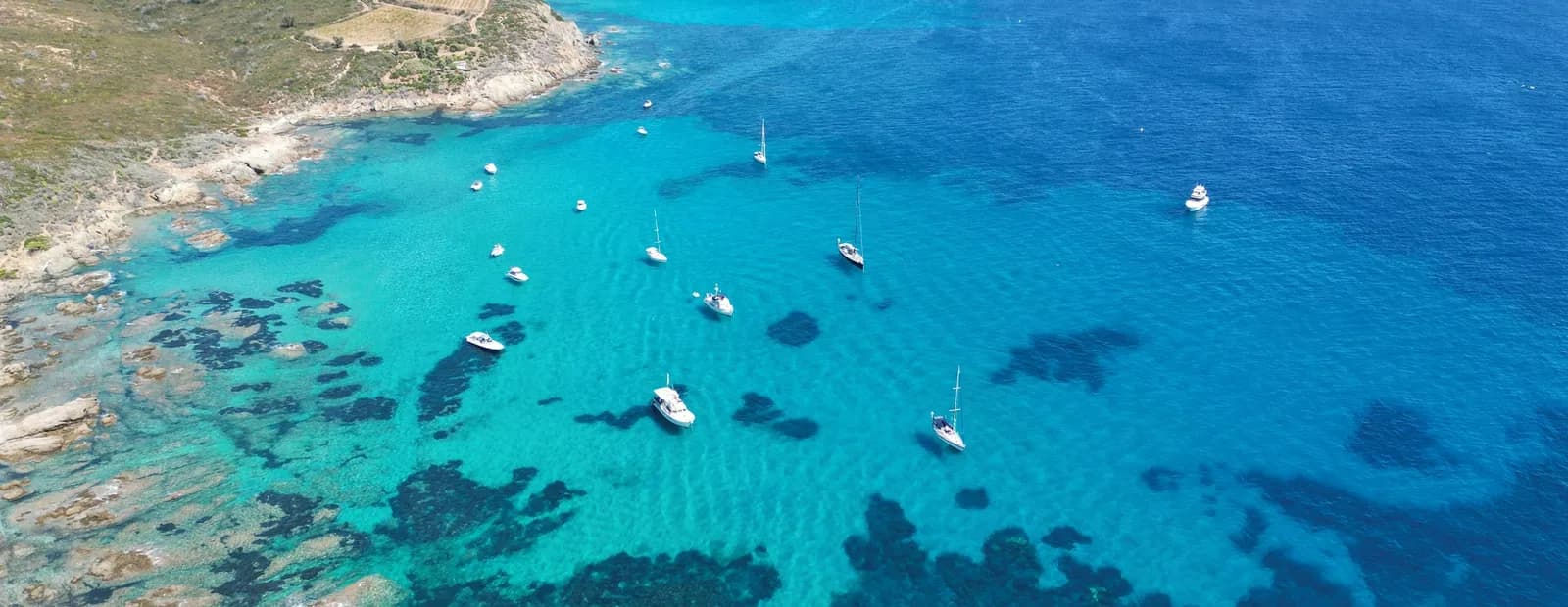 Voiliers et bateaux à moteur au mouillage dans une baie aux eaux turquoise, vue du ciel