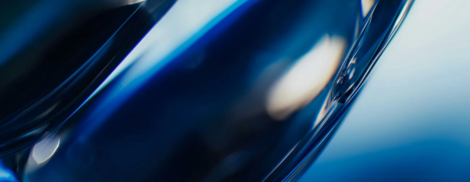 Gros plan sur des courbes de verre translucide bleu nuit, traversées de reflets clairs sur un fond bleu flou