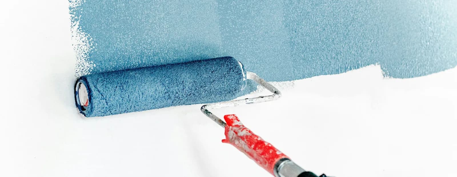 Rouleau à peinture appliquant une couche bleu-gris sur un mur blanc en cours de rénovation