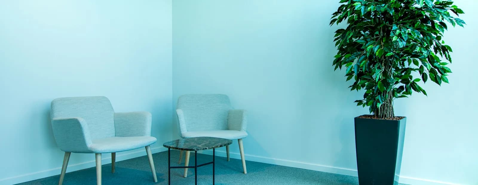 Deux fauteuils en tissu clair et une table basse en marbre dans un coin de bureau, à côté d’une plante en pot