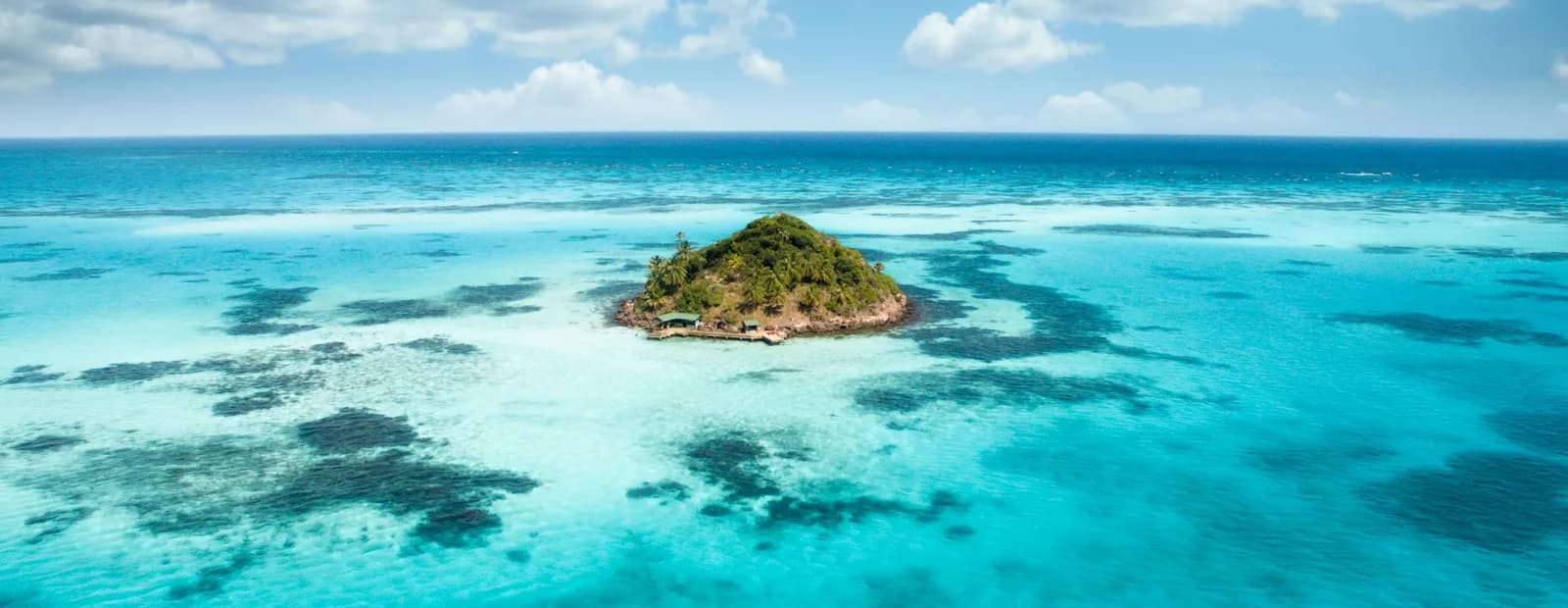 Petit îlot boisé au milieu d’une mer turquoise peu profonde, sous un ciel bleu parsemé de nuages blancs