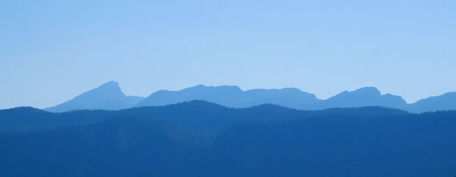 Crêtes de montagnes superposées qui s’estompent dans une brume bleue, sous un ciel clair