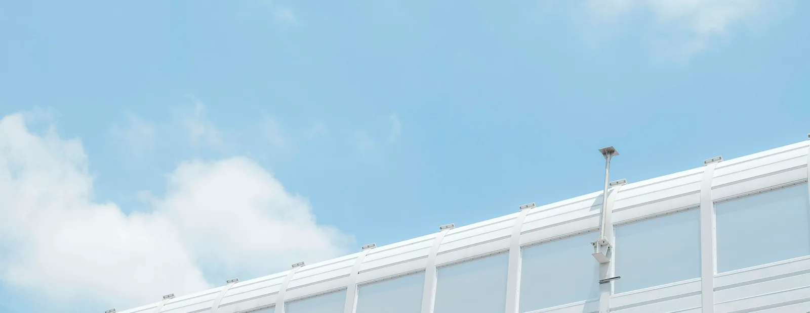 Arête d’un bâtiment blanc aux lignes nettes sous un ciel bleu clair parsemé de nuages.