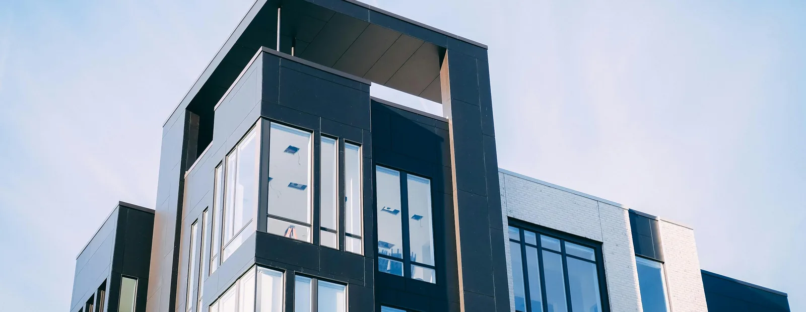 Immeuble d’habitation moderne en contre-plongée, façade noire et blanche à larges baies vitrées sous un ciel bleu