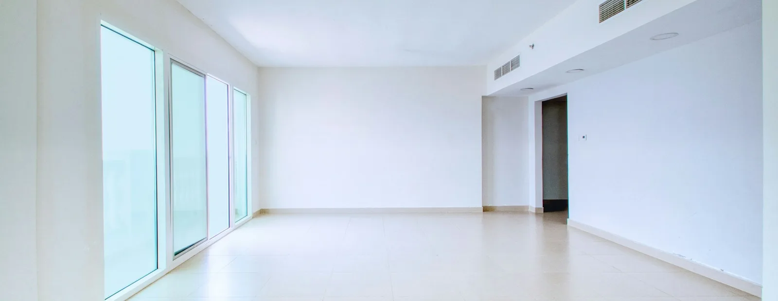 Grande pièce vide aux murs blancs et au carrelage clair, éclairée par une rangée de baies vitrées, telle qu’un lot remis en état avant relocation