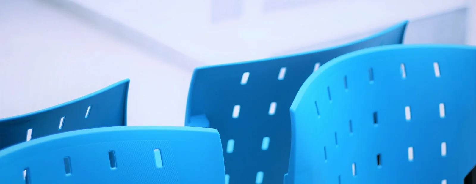 Rangée de fauteuils bleus perforés dans une salle d’attente lumineuse aux murs blancs