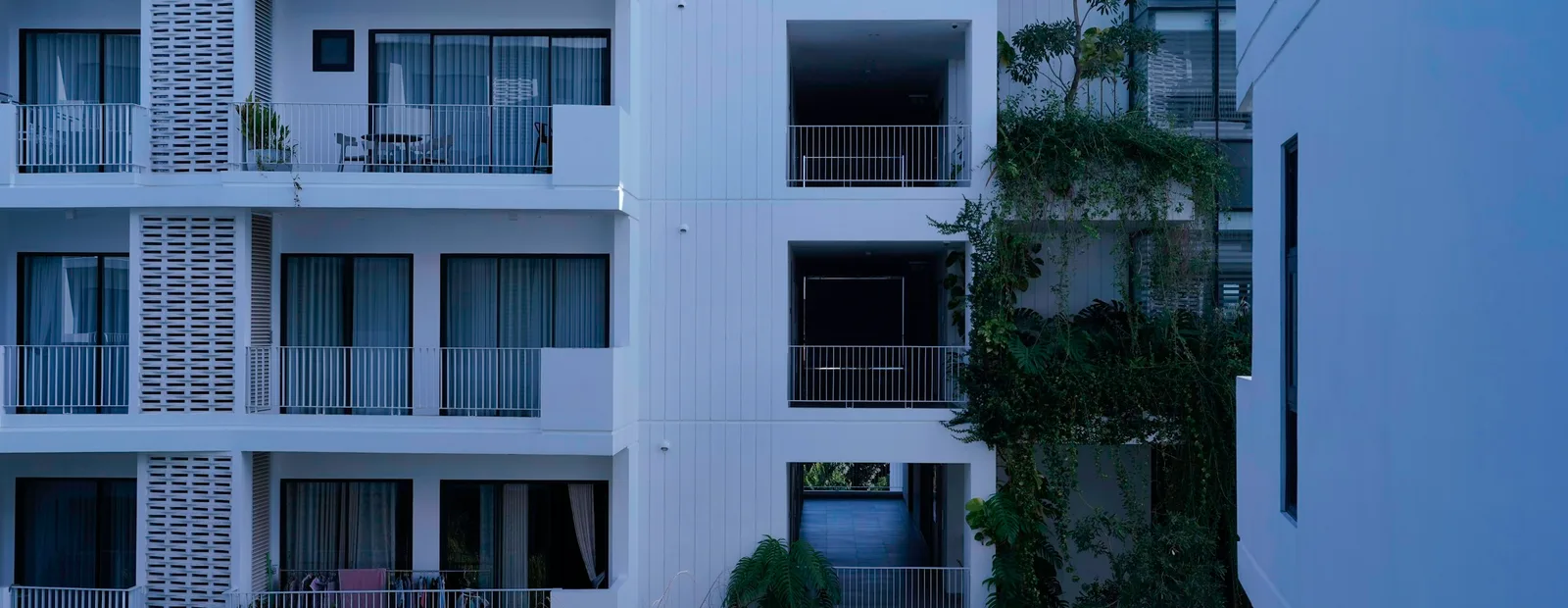 Façades blanches d’immeubles d’habitation récents avec balcons à garde-corps et végétation grimpante entre deux bâtiments