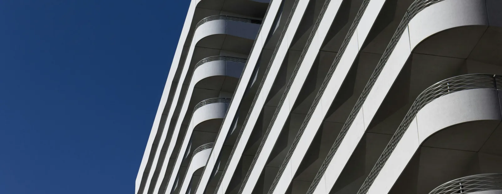 Contre-plongée sur la façade blanche d’un immeuble d’habitation aux balcons arrondis, sous un ciel bleu profond
