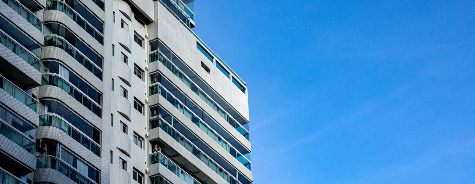 Façade blanche d’un immeuble à balcons vitrés, sous un ciel bleu dégagé
