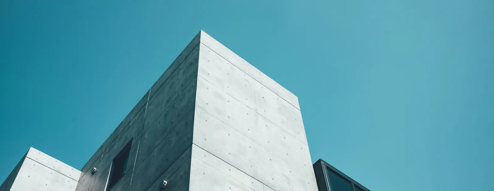 Façade en béton d’un immeuble contemporain photographiée en contre-plongée sur un ciel bleu uni